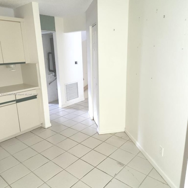 interior space featuring light tile patterned floors, light countertops, visible vents, white cabinets, and baseboards