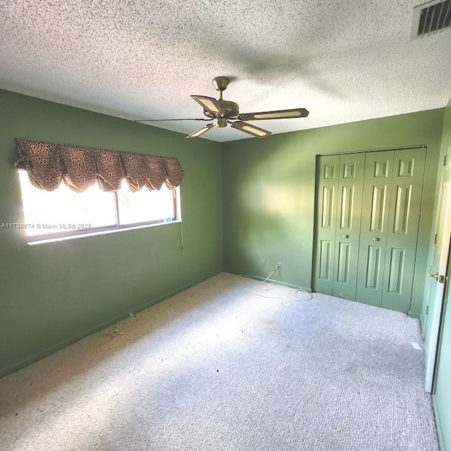 carpeted spare room featuring visible vents, a textured ceiling, and a ceiling fan