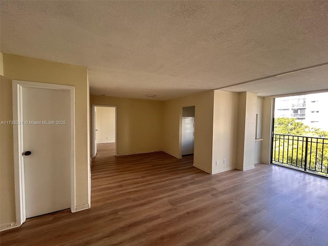 unfurnished room featuring a wall of windows, wood-type flooring, and a textured ceiling