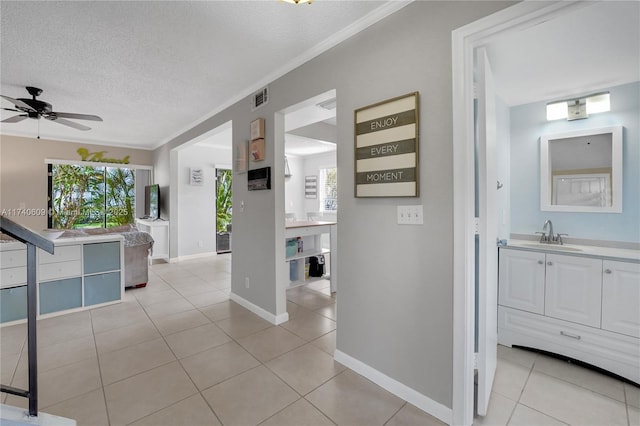 corridor featuring sink, light tile patterned floors, a wealth of natural light, ornamental molding, and a textured ceiling