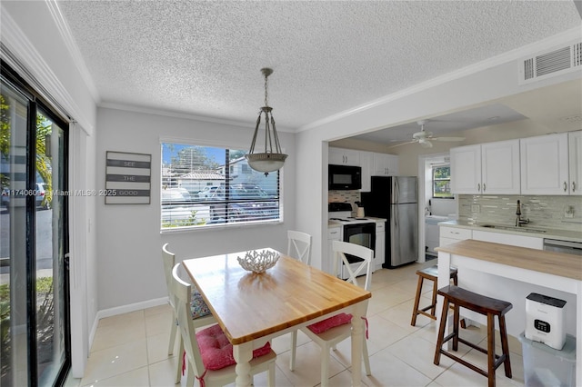 tiled dining space featuring sink, a textured ceiling, ornamental molding, and ceiling fan