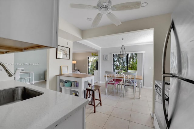 kitchen featuring sink, decorative light fixtures, light tile patterned floors, stainless steel fridge, and stove