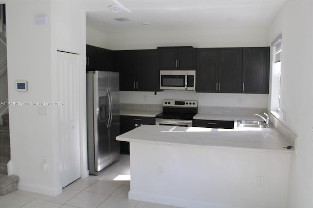 kitchen with stainless steel appliances, sink, light tile patterned floors, and kitchen peninsula