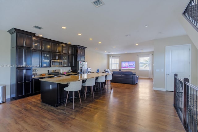 kitchen featuring appliances with stainless steel finishes, dark hardwood / wood-style floors, a kitchen breakfast bar, a kitchen island with sink, and light stone counters