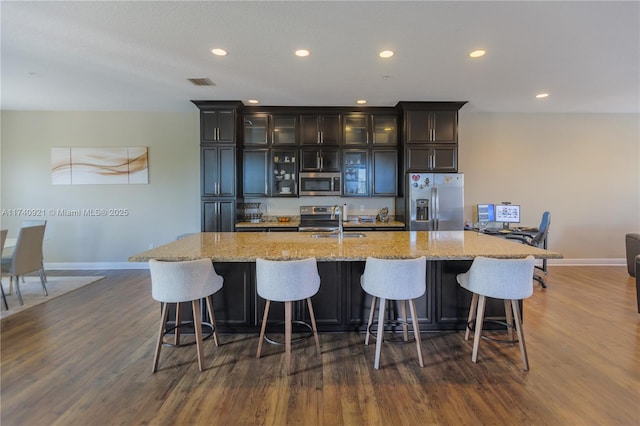 kitchen with a spacious island, appliances with stainless steel finishes, dark hardwood / wood-style flooring, and light stone counters