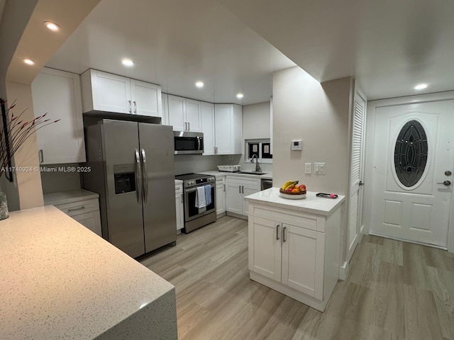 kitchen featuring sink, white cabinetry, stainless steel appliances, light hardwood / wood-style floors, and light stone countertops