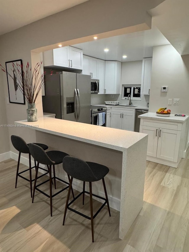 kitchen featuring a breakfast bar, sink, appliances with stainless steel finishes, kitchen peninsula, and white cabinets