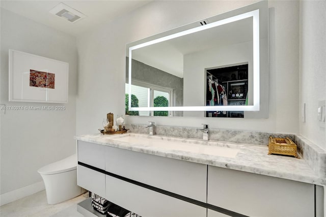 bathroom featuring baseboards, visible vents, toilet, a spacious closet, and vanity