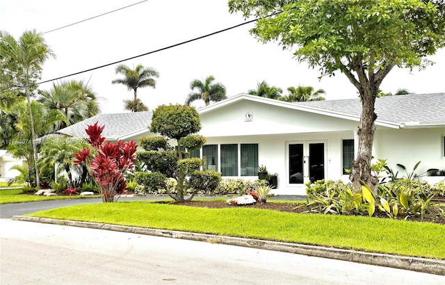 view of front of property featuring a front yard, roof with shingles, and stucco siding