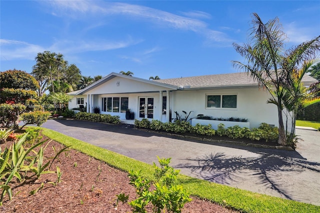 ranch-style house with driveway, roof with shingles, and stucco siding