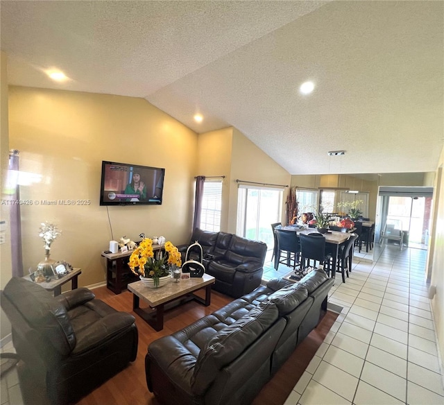 living room featuring a healthy amount of sunlight, light tile patterned floors, vaulted ceiling, and a textured ceiling