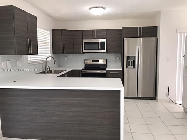 kitchen with light countertops, appliances with stainless steel finishes, a sink, dark brown cabinetry, and a peninsula