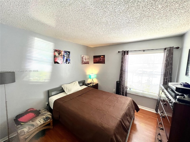 bedroom with a textured ceiling, baseboards, and wood finished floors