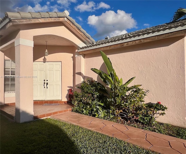 entrance to property featuring a tiled roof and stucco siding