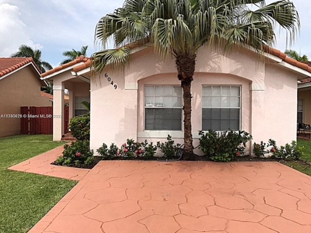 exterior space featuring a tile roof, a lawn, fence, and stucco siding