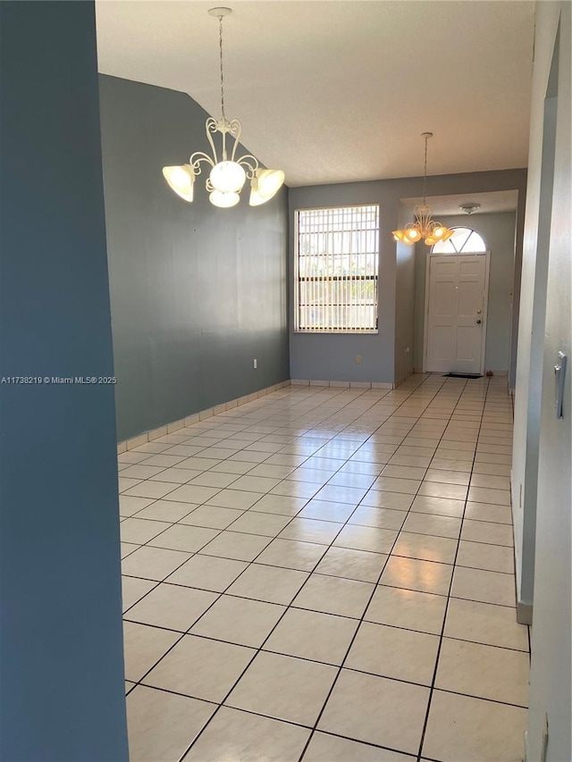 unfurnished room featuring light tile patterned flooring, lofted ceiling, and a notable chandelier