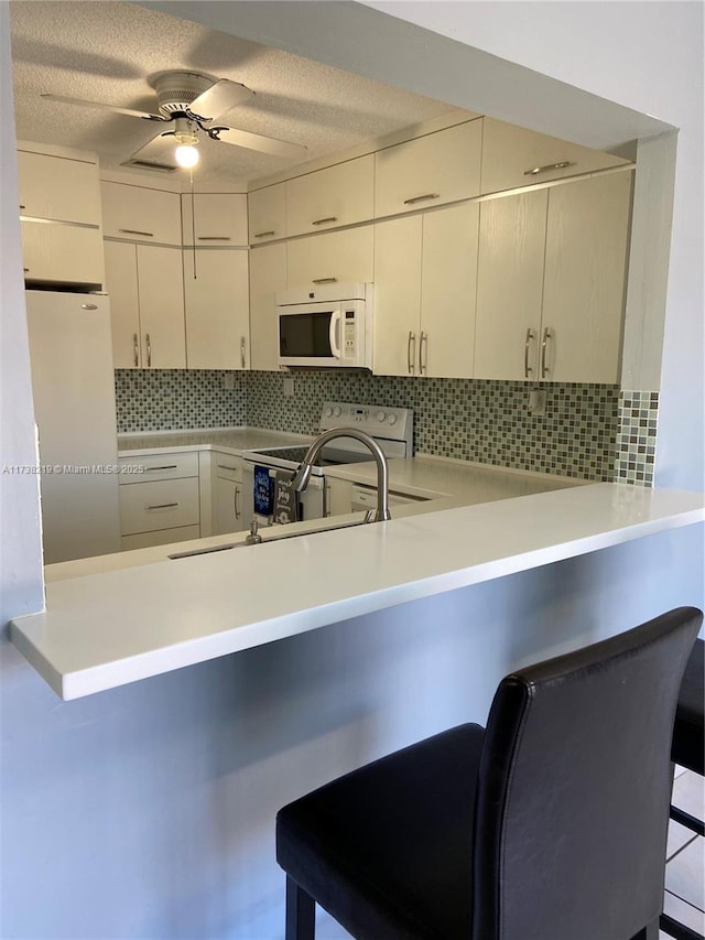 kitchen with backsplash, a kitchen breakfast bar, ceiling fan, kitchen peninsula, and white appliances