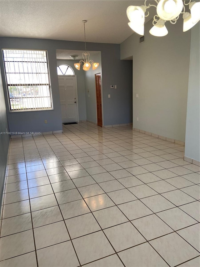 tiled empty room featuring a textured ceiling and an inviting chandelier