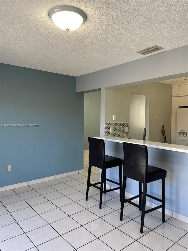 kitchen featuring a kitchen bar, decorative backsplash, white fridge with ice dispenser, light tile patterned floors, and kitchen peninsula