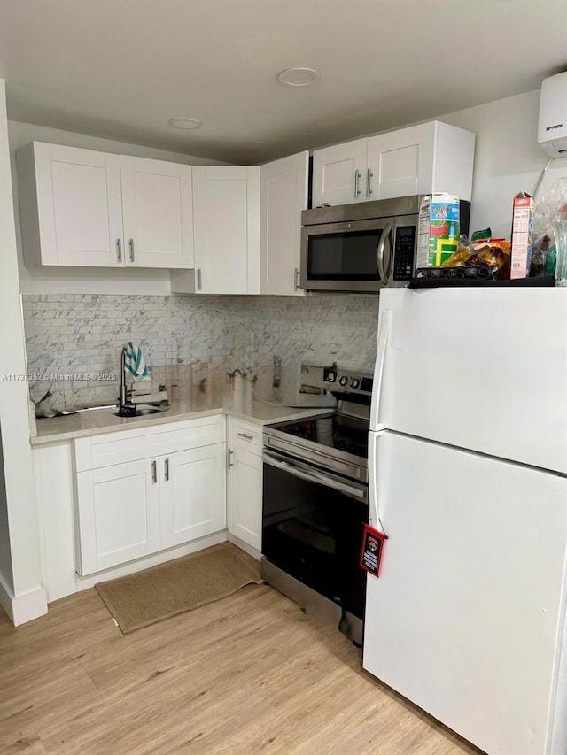 kitchen featuring sink, light wood-type flooring, appliances with stainless steel finishes, white cabinets, and backsplash