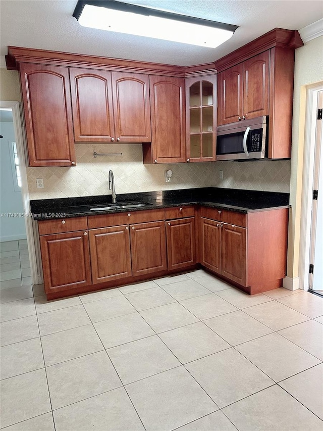 kitchen featuring dark stone countertops, sink, light tile patterned floors, and decorative backsplash