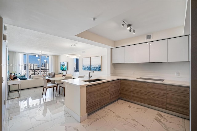 kitchen featuring sink, white cabinets, black electric cooktop, decorative light fixtures, and kitchen peninsula