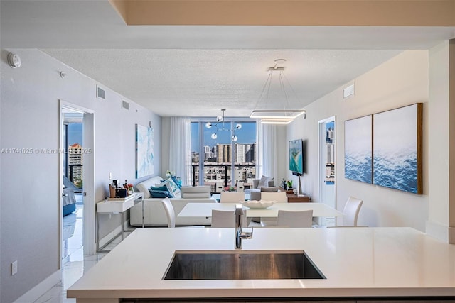 kitchen featuring sink, an inviting chandelier, a textured ceiling, a center island with sink, and pendant lighting