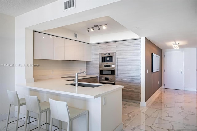 kitchen with a kitchen bar, sink, white cabinetry, kitchen peninsula, and stainless steel double oven