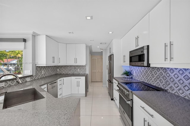 2816 NE 24th Pl, Fort Lauderdale, FL 33305 - kitchen featuring stainless steel appliances, dark stone counters, light tile patterned floors, decorative backsplash, and white cabinetry