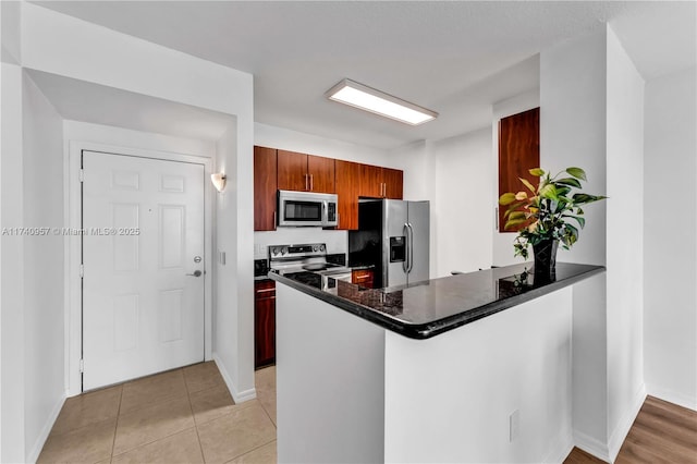 kitchen with dark stone countertops, light tile patterned floors, kitchen peninsula, and appliances with stainless steel finishes