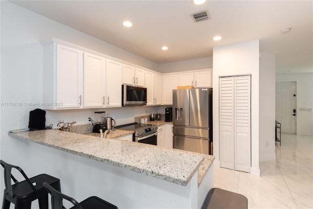 kitchen with appliances with stainless steel finishes, white cabinets, light stone counters, and kitchen peninsula