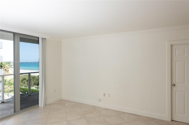 unfurnished room with light tile patterned flooring, a view of the beach, a wall of windows, ornamental molding, and a water view