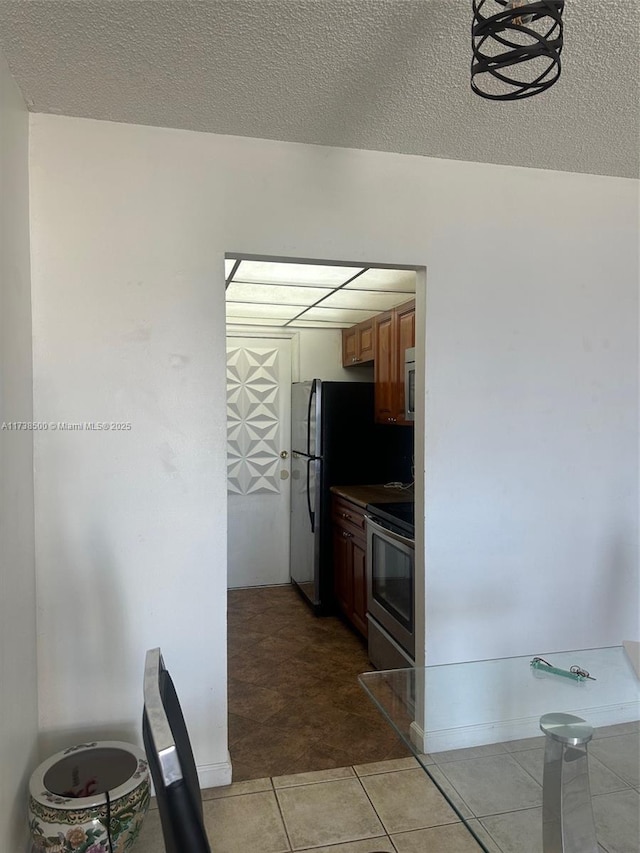 kitchen featuring light tile patterned floors, stainless steel electric stove, a textured ceiling, and black fridge