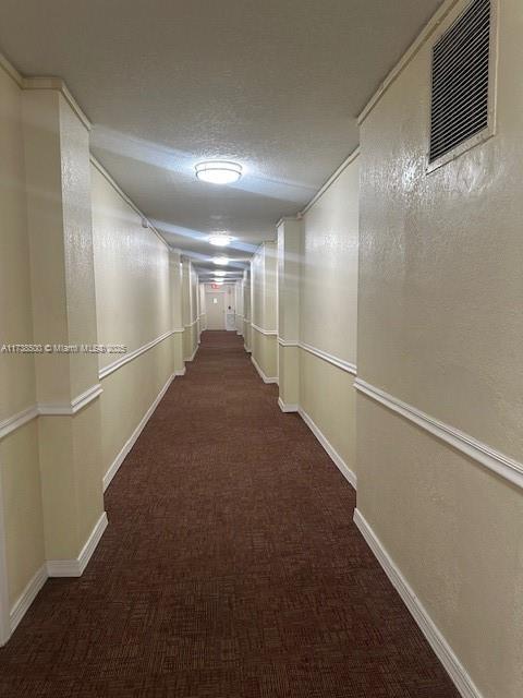 corridor featuring a textured ceiling and dark carpet