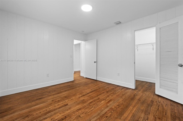 unfurnished bedroom featuring dark wood-type flooring, a spacious closet, and a closet