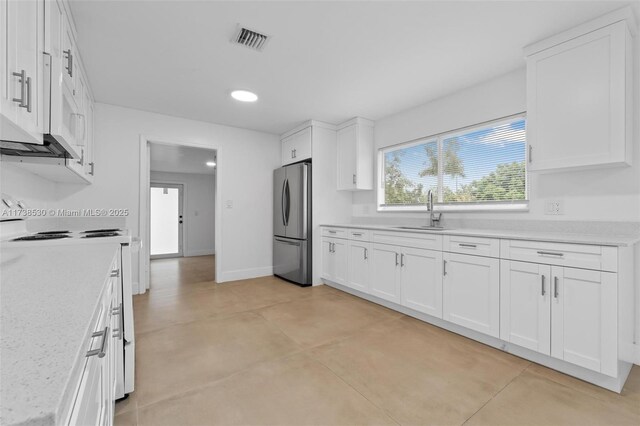 kitchen featuring sink, light stone counters, range, stainless steel refrigerator, and white cabinets