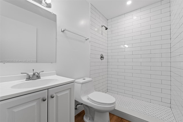 bathroom featuring vanity, tiled shower, hardwood / wood-style floors, and toilet