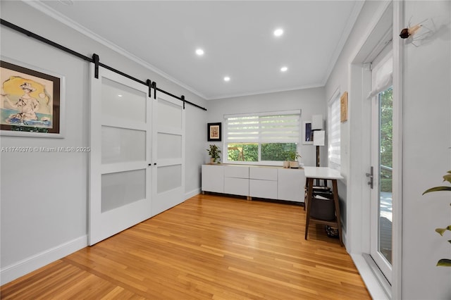 interior space featuring ornamental molding, a barn door, and light wood-type flooring