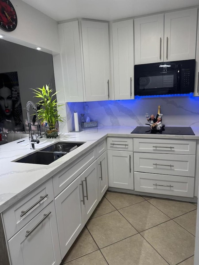 kitchen with white cabinetry, black appliances, light tile patterned flooring, and a sink