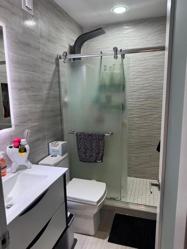 bathroom with a shower stall, tile walls, vanity, and toilet