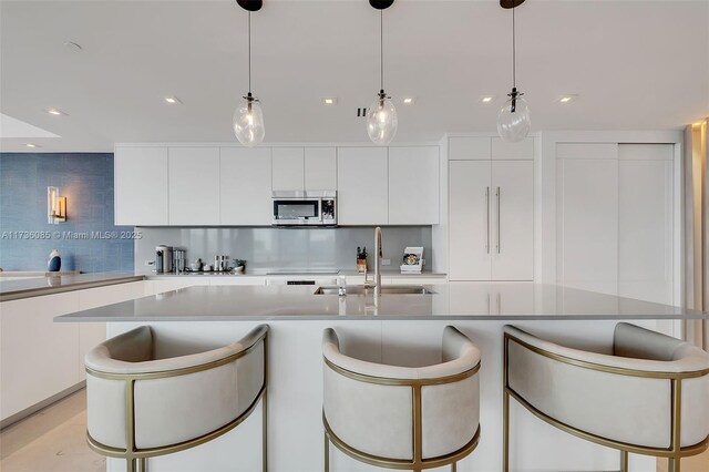 68 SE 6th St Unit 3911, Miami, FL 33131 - kitchen with white cabinetry, sink, decorative light fixtures, and an island with sink