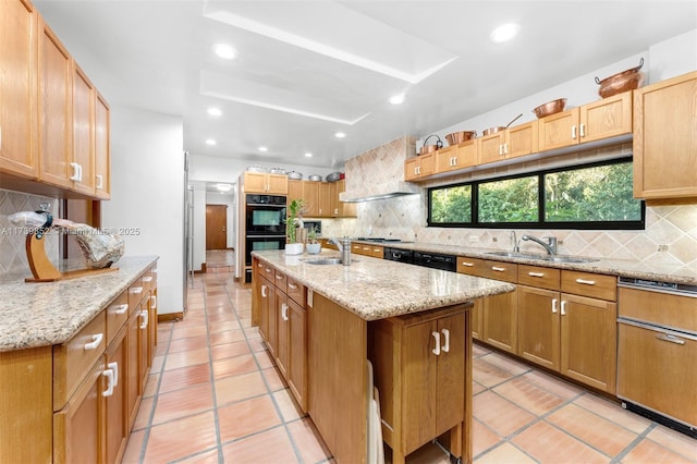 kitchen featuring tasteful backsplash, sink, light stone counters, black appliances, and a center island with sink