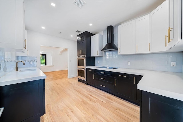 kitchen with wall chimney range hood, visible vents, light countertops, and a sink