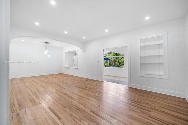 empty room featuring light wood-style floors, baseboards, built in shelves, and arched walkways