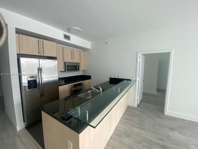 kitchen with appliances with stainless steel finishes, light brown cabinetry, sink, light hardwood / wood-style floors, and kitchen peninsula