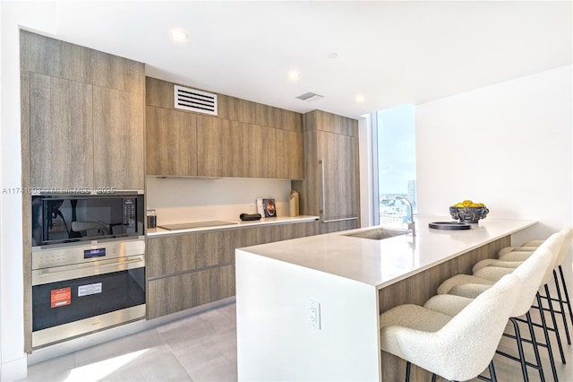 kitchen with sink, a breakfast bar area, black appliances, and an island with sink