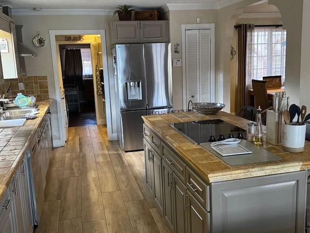 kitchen with stainless steel fridge, ornamental molding, tile countertops, and light wood-type flooring