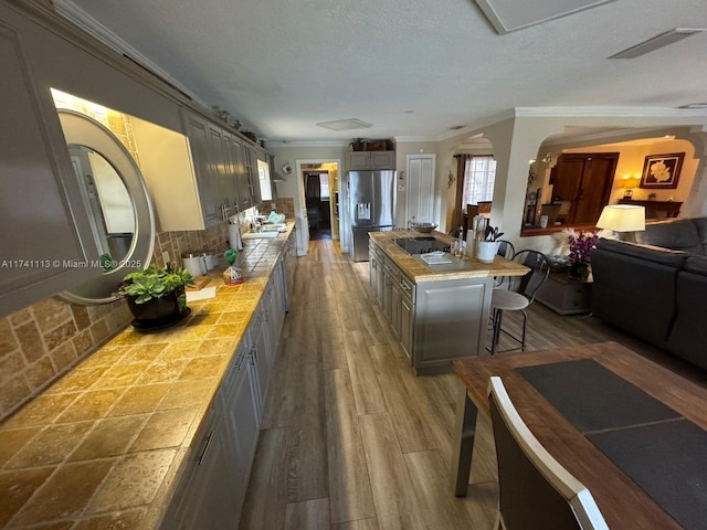 kitchen with a kitchen island, a breakfast bar, tile countertops, stainless steel fridge, and decorative backsplash