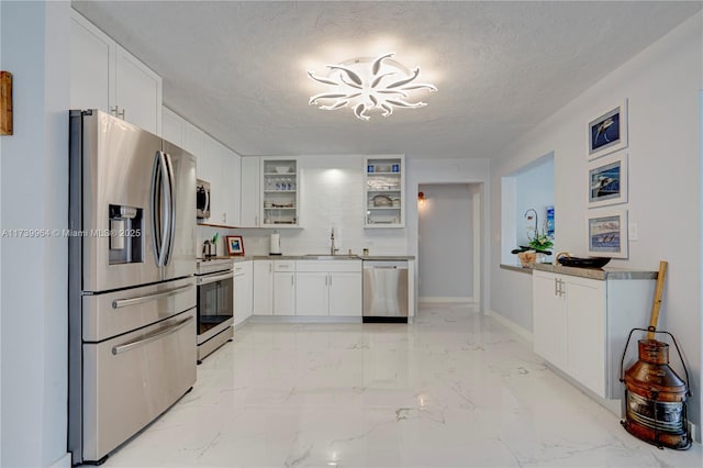 kitchen with stainless steel appliances, a sink, white cabinetry, light countertops, and glass insert cabinets