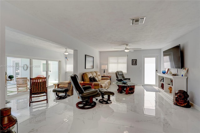 living area with marble finish floor, visible vents, ceiling fan, a textured ceiling, and baseboards